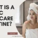 A person wrapped in a white towel with a matching hair turban looking into a bathroom mirror and touching their face; large text to the left asks "WHAT IS A BASIC SKINCARE ROUTINE?".