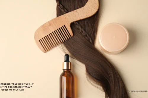A top-down view of hair care essentials featuring a long strand of wavy brunette hair with a small braid, a wooden wide-tooth comb, an amber glass dropper bottle, and a round tan cosmetic jar on a neutral background.